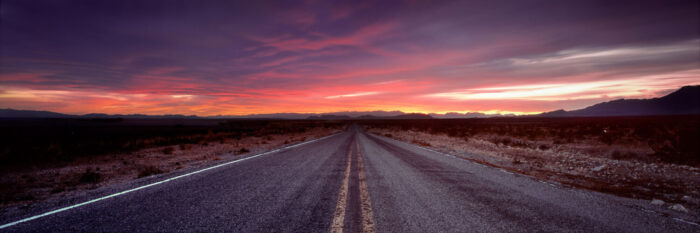 Long straight US road leading to sunset