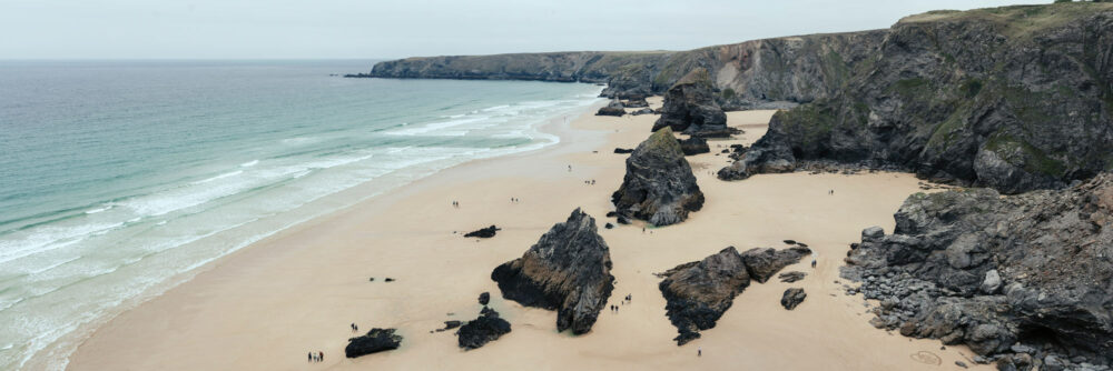 A panoramic print of Bedruthan beach as people walk around