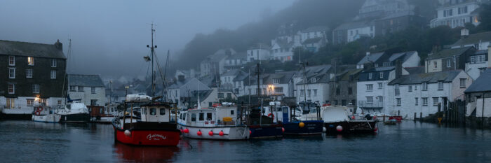 Panorama of Polperro Harbour and fishing boats during morning mist along the south west coast path in Cornwall