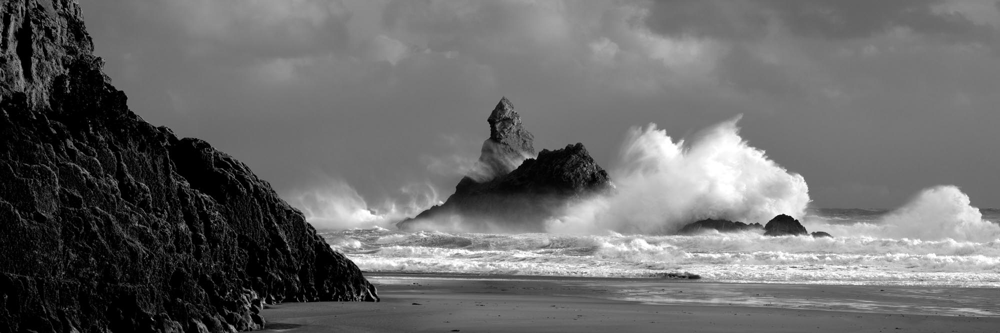 Panorama of story waves crashing against Church Rock on the Pembrokeshire coast b&w