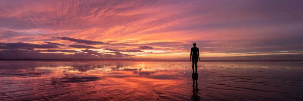 Panorama of Antony Gormley Another place sculptures at sunset on Crosby Beach in Merseyside