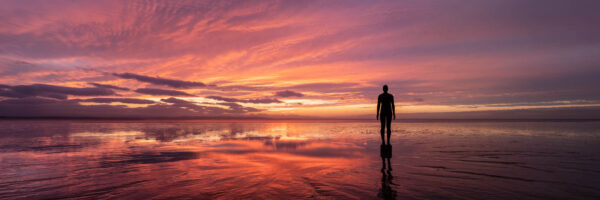 Panorama of Antony Gormley Another place sculptures at sunset on Crosby Beach in Merseyside