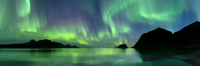 Panorama of Haukland beach with the Aurora Borealis above in the arctic circle