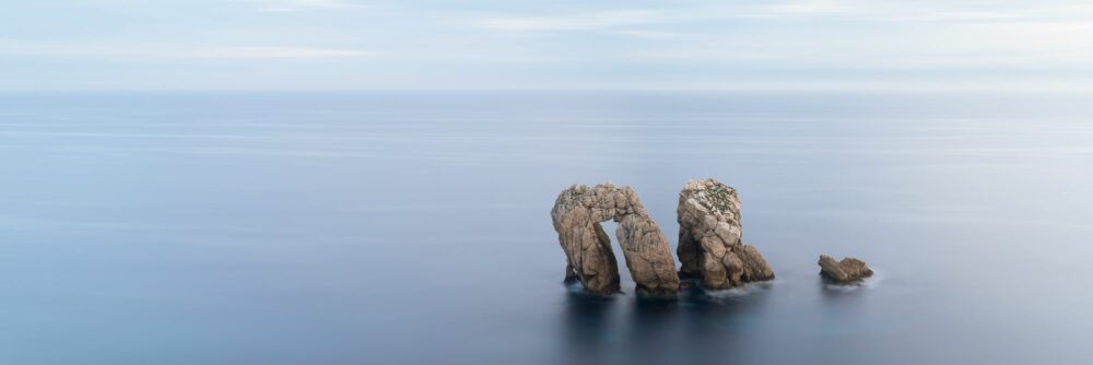 Panorama of serene blue water surround the Urro del Manzano Arch in Spain